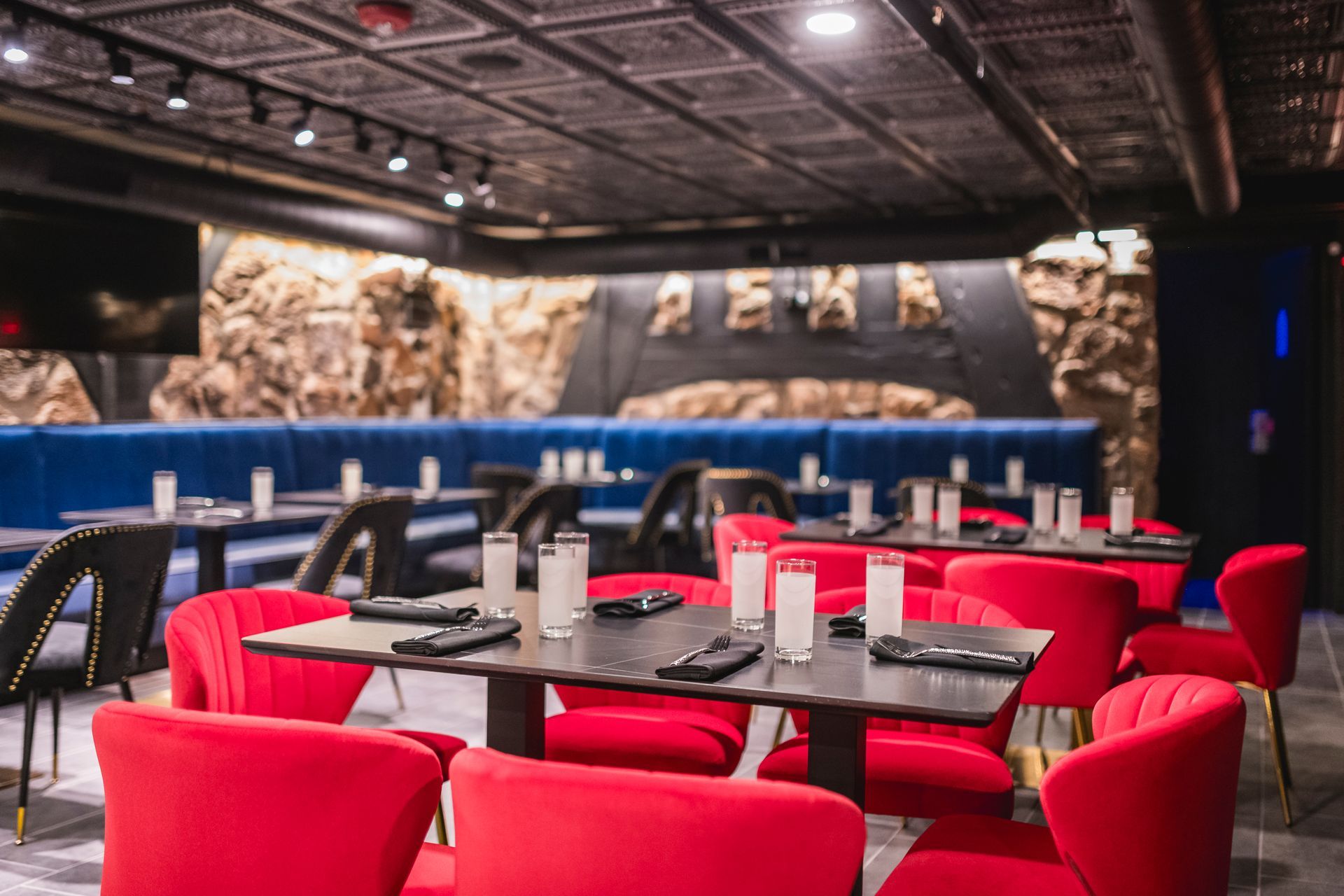 Modern lounge dining area with red chairs, black tables, and a stone wall backdrop