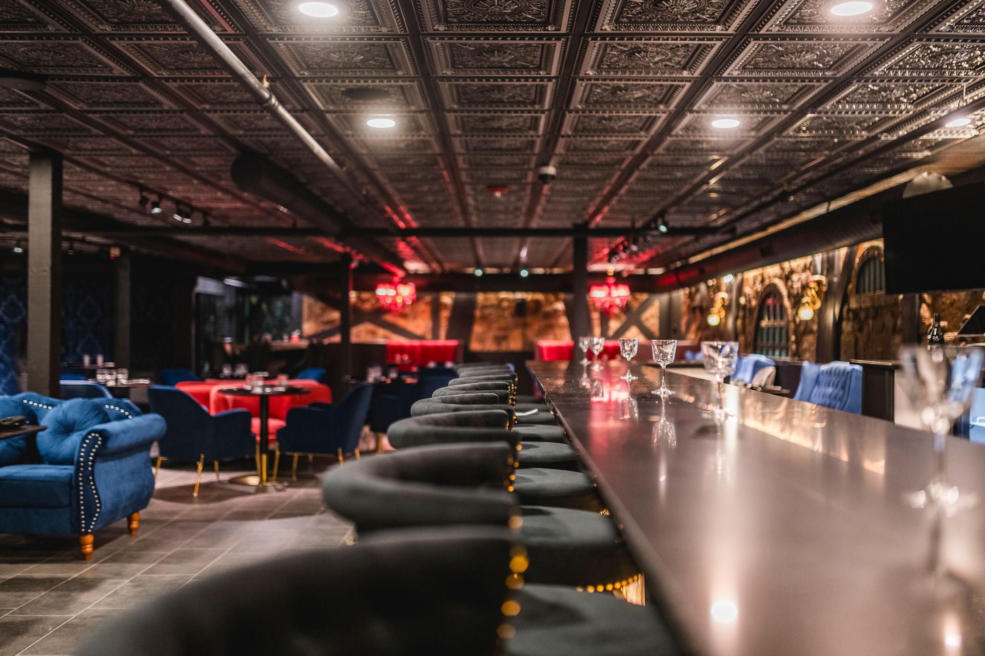 Stylish nightclub lounge with blue and red seating, mirrored ceiling, and a long metallic bar