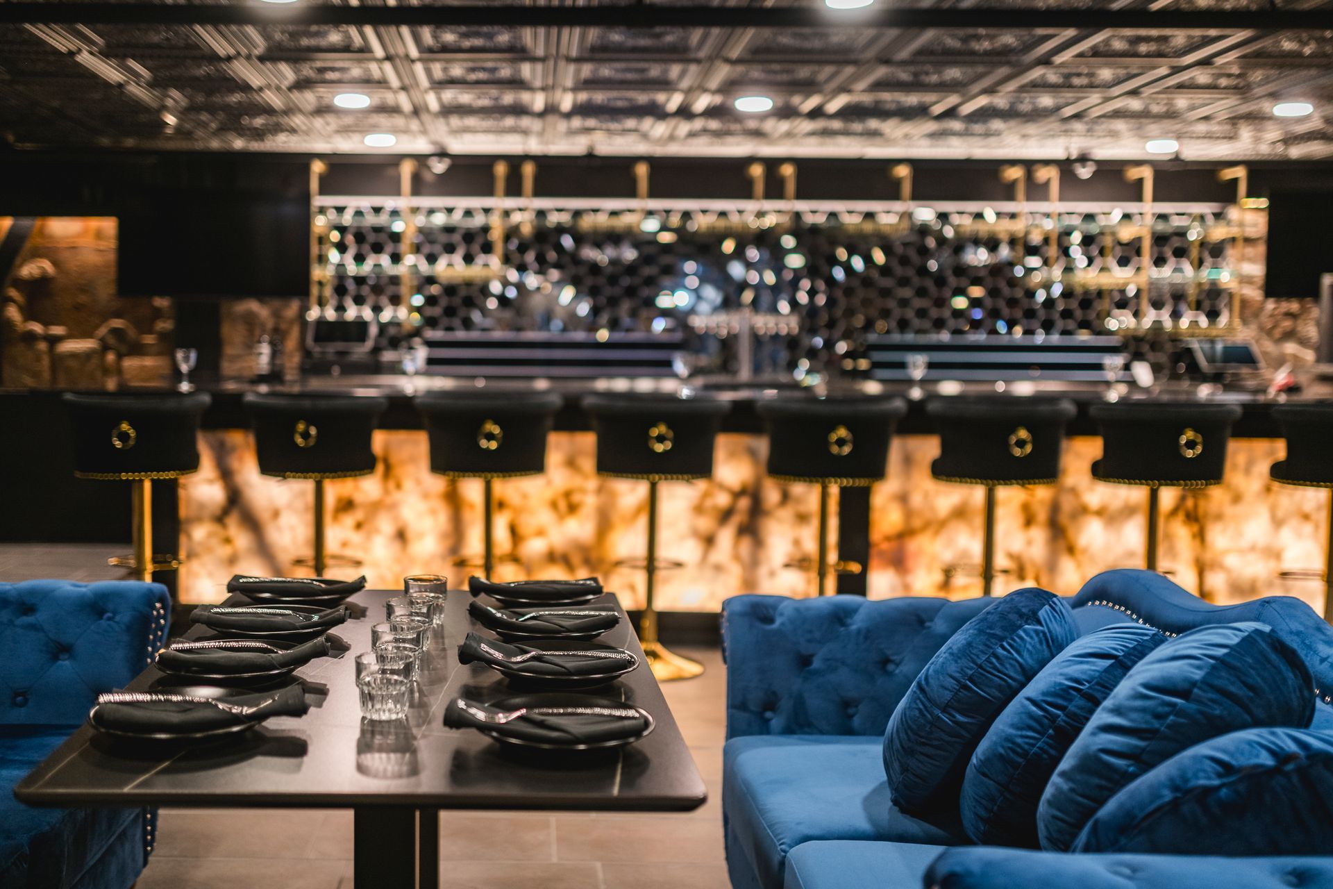 Stylish restaurant interior with blue velvet seating, set dining tables, and a warmly lit bar backdrop