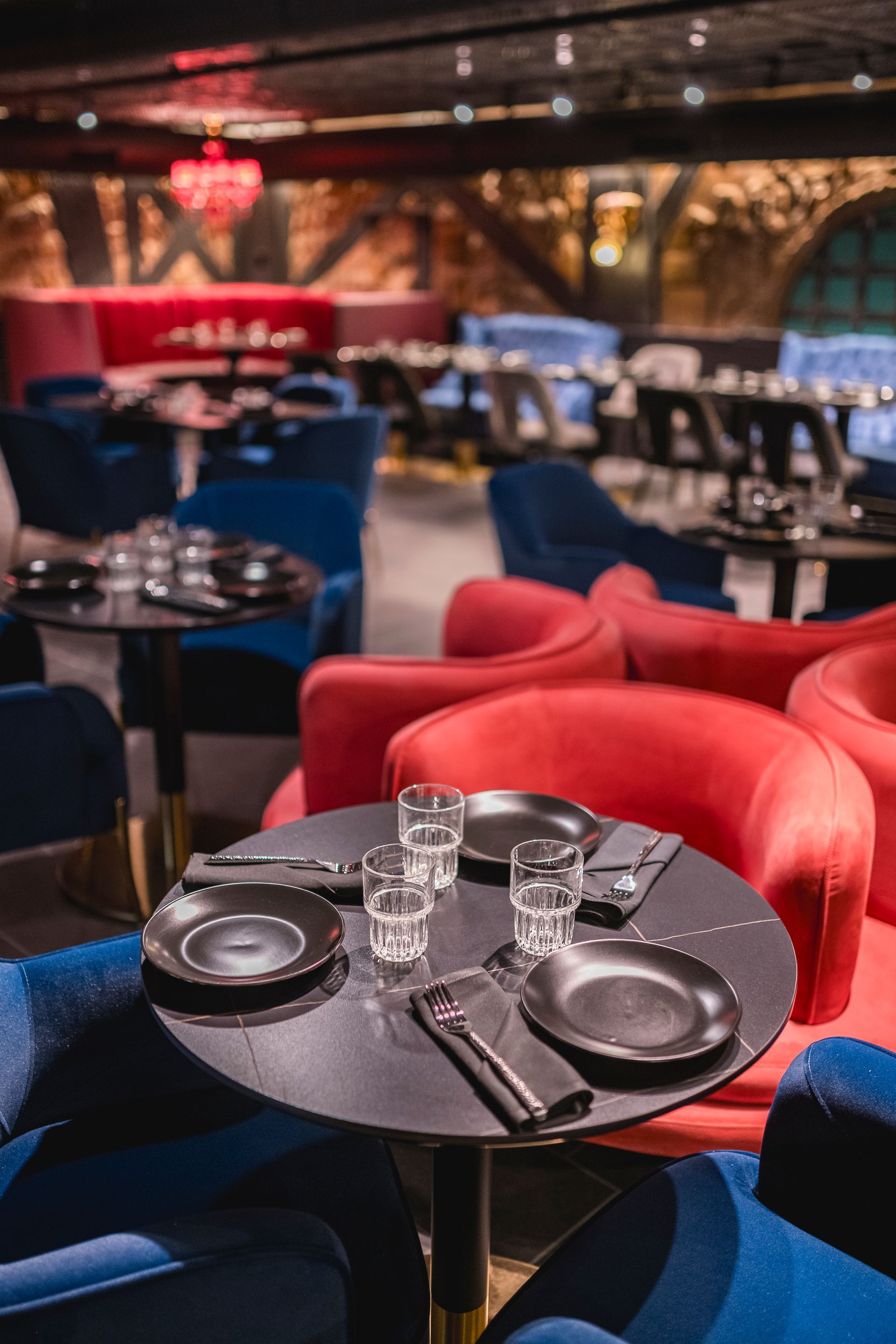 Cozy lounge restaurant with red armchairs and set black tables under warm ambient lighting