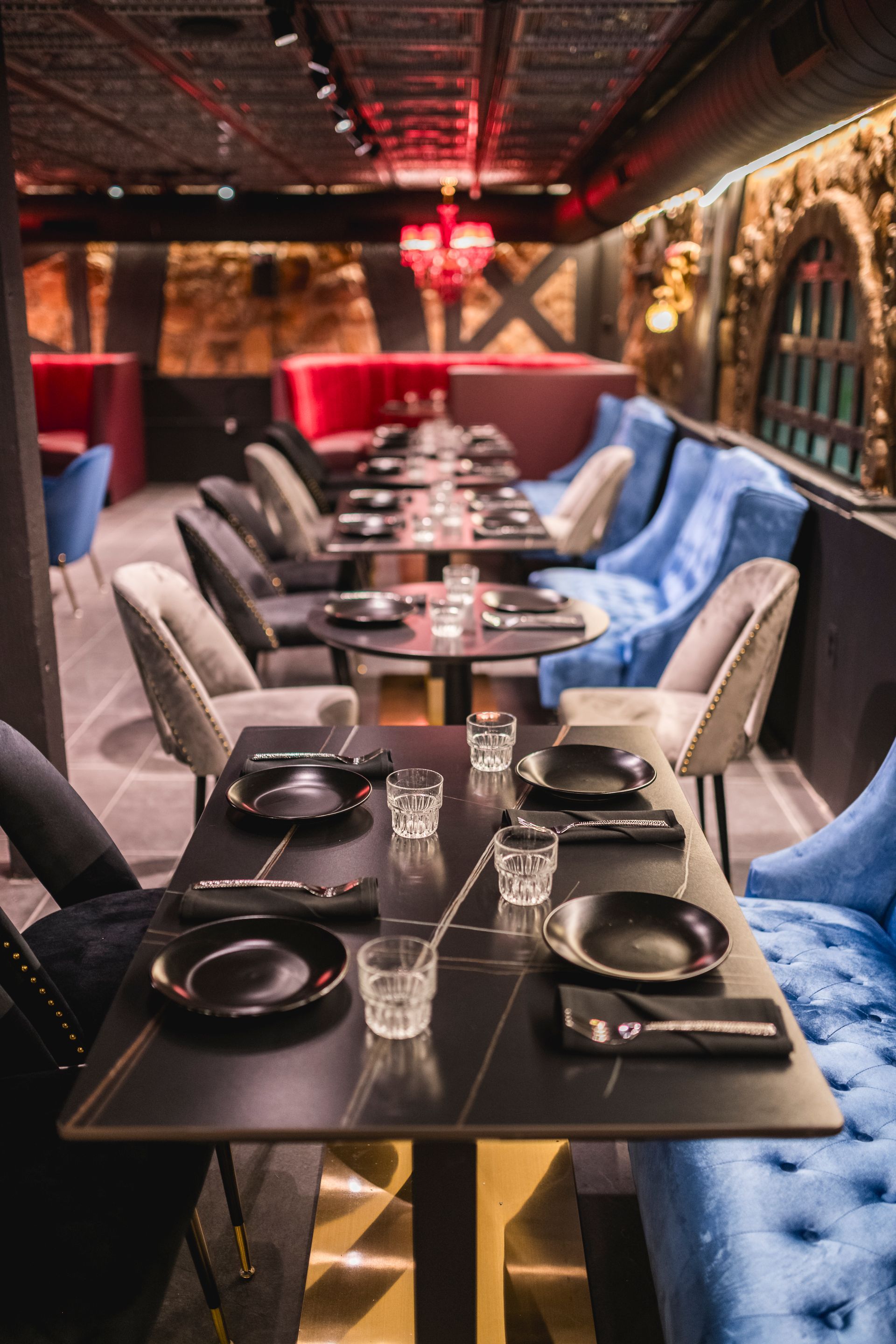 Dimly lit restaurant dining room with black tables, blue chairs, and red booth seating