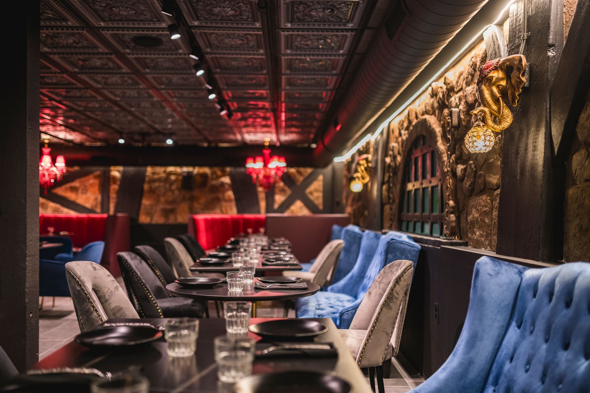 Elegant dimly lit lounge with blue velvet chairs, long table, and ornate gold wall decor