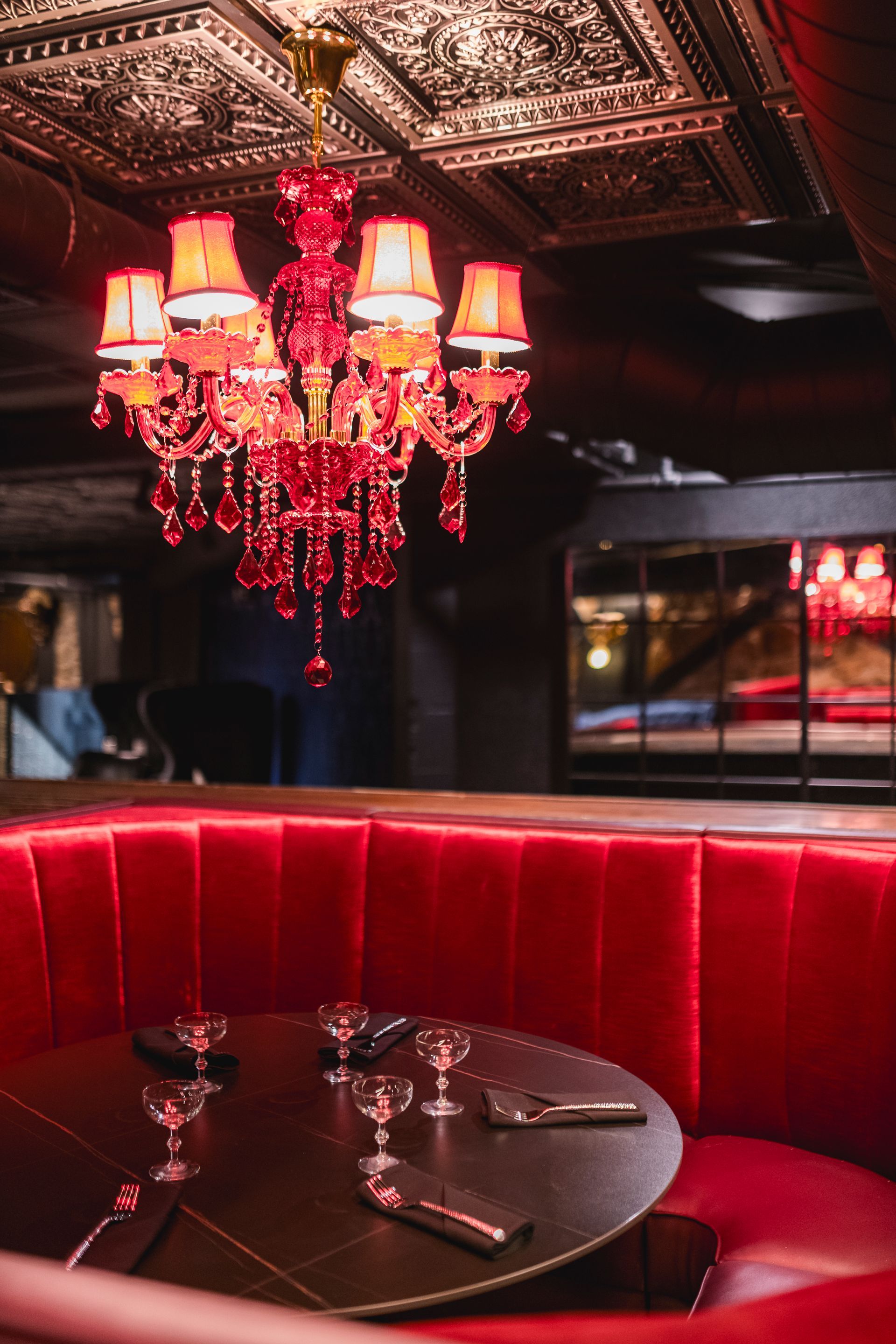 Red velvet booth under a red chandelier in a dimly lit lounge with a set dining table
