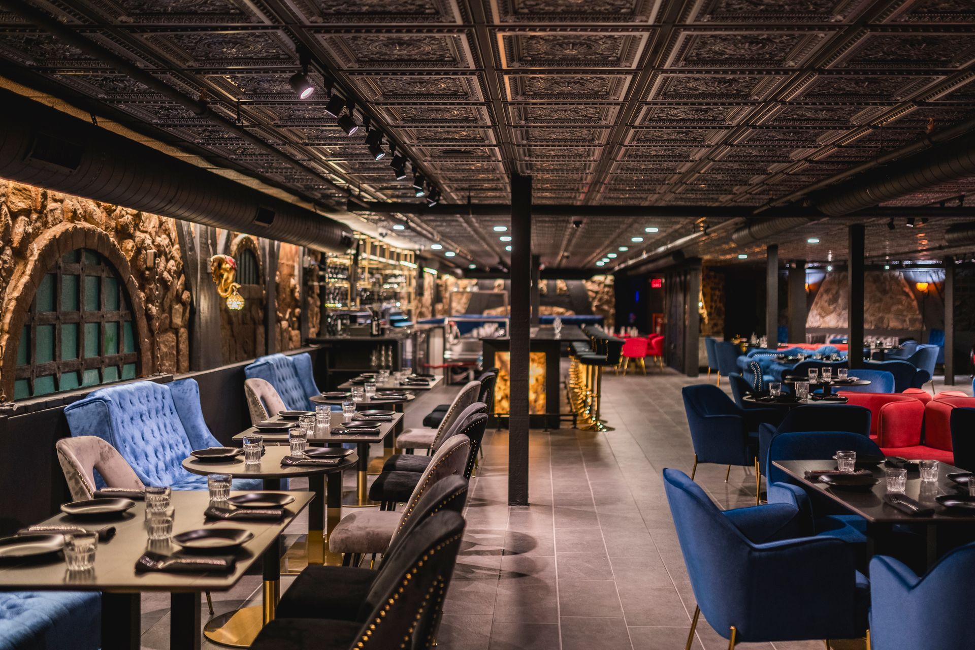 Upscale restaurant dining room with patterned ceiling, blue and red velvet chairs, and neatly set tables