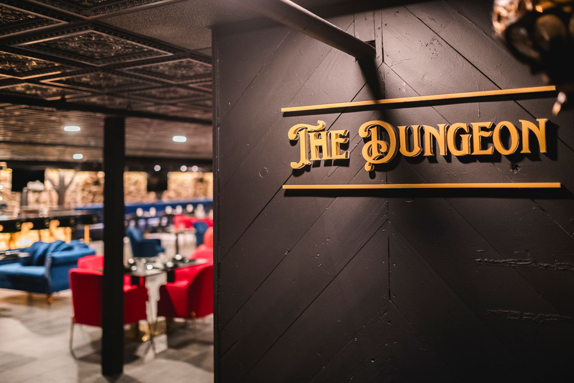 “The Dungeon” sign on a black wall beside a restaurant interior with red chairs and blue booths