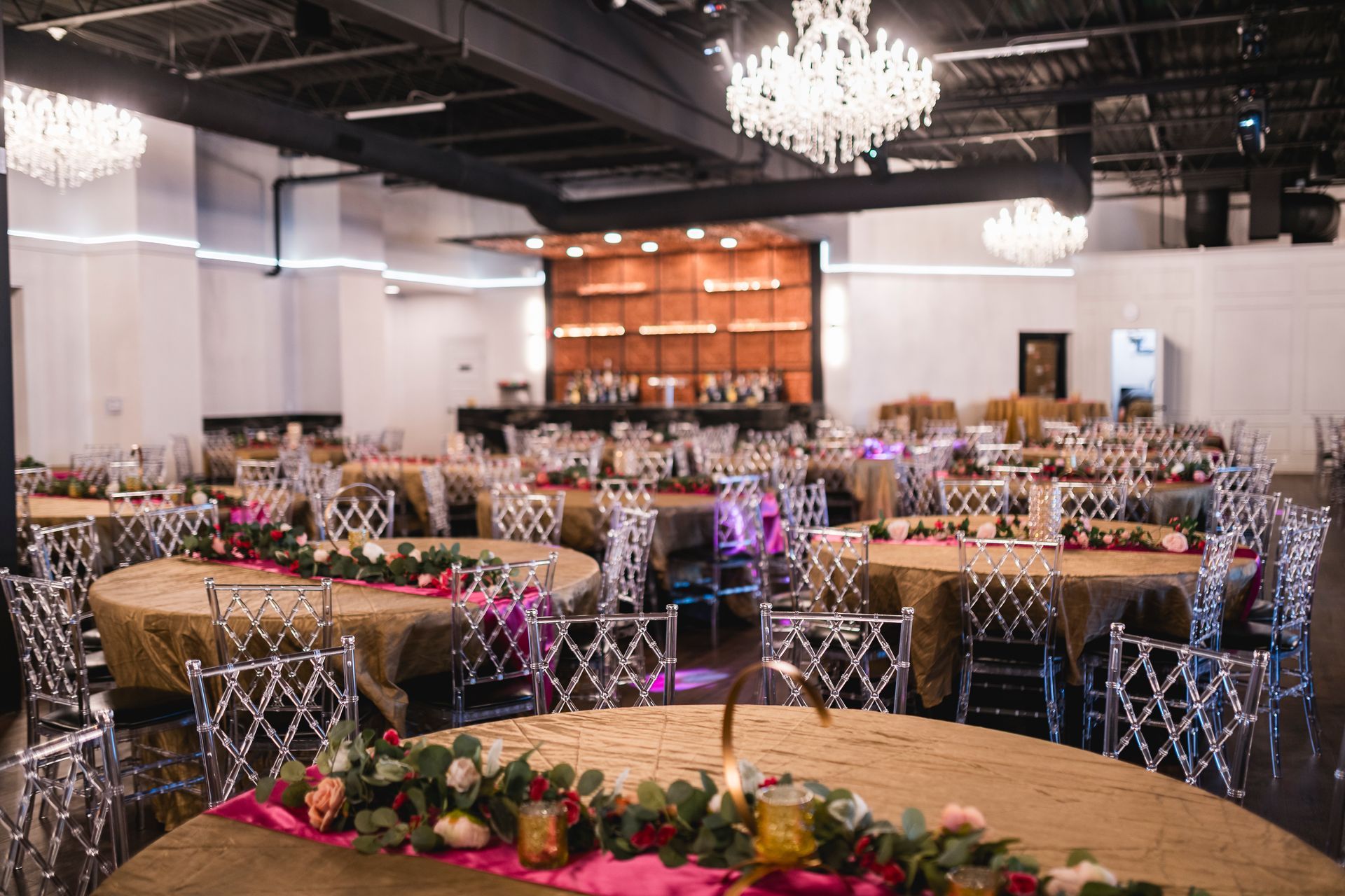 Elegant banquet hall with round tables, floral centerpieces, and chandeliers under a dark ceiling