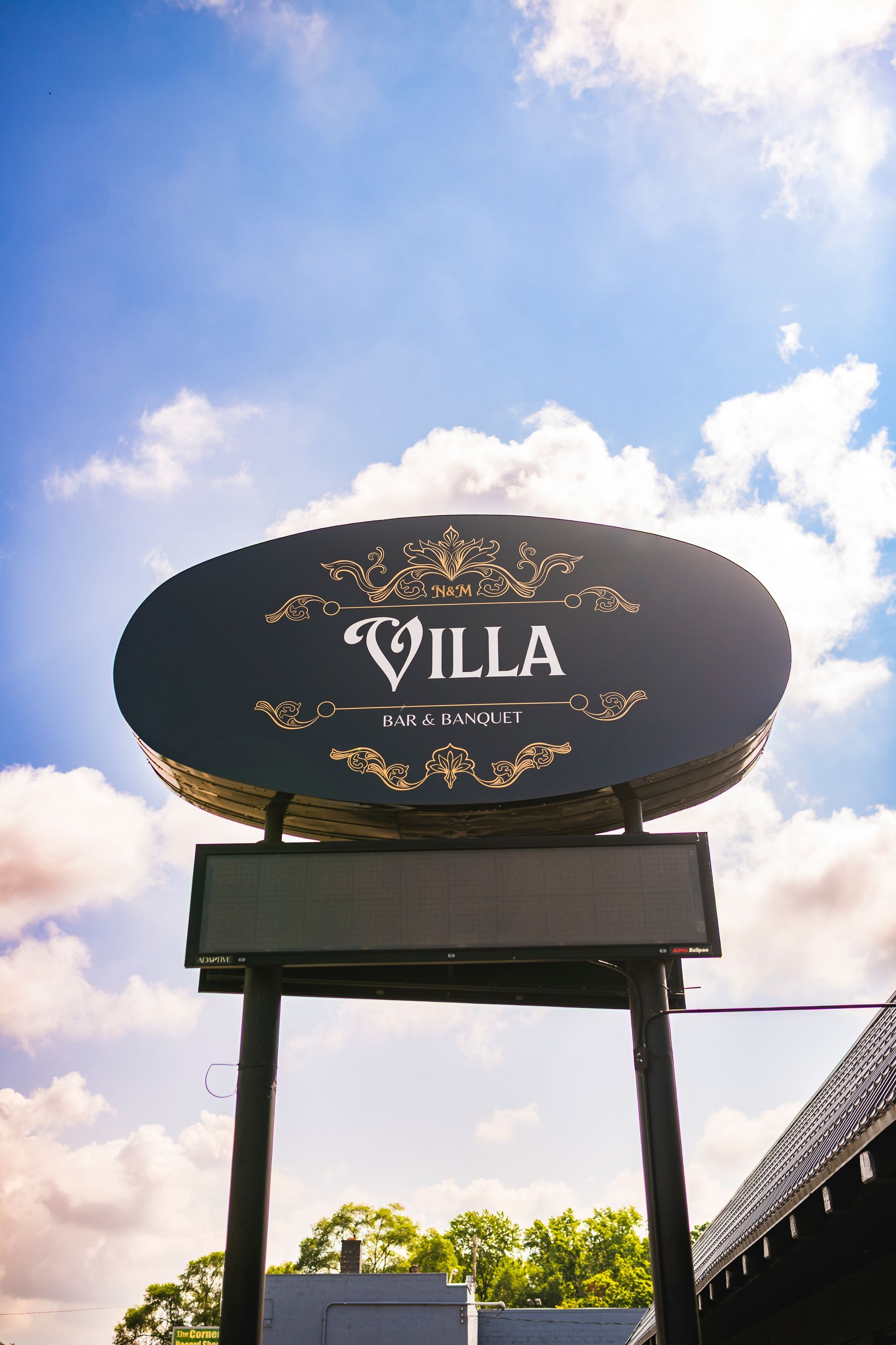 Black oval VILLA sign on a tall stand against a blue sky with clouds
