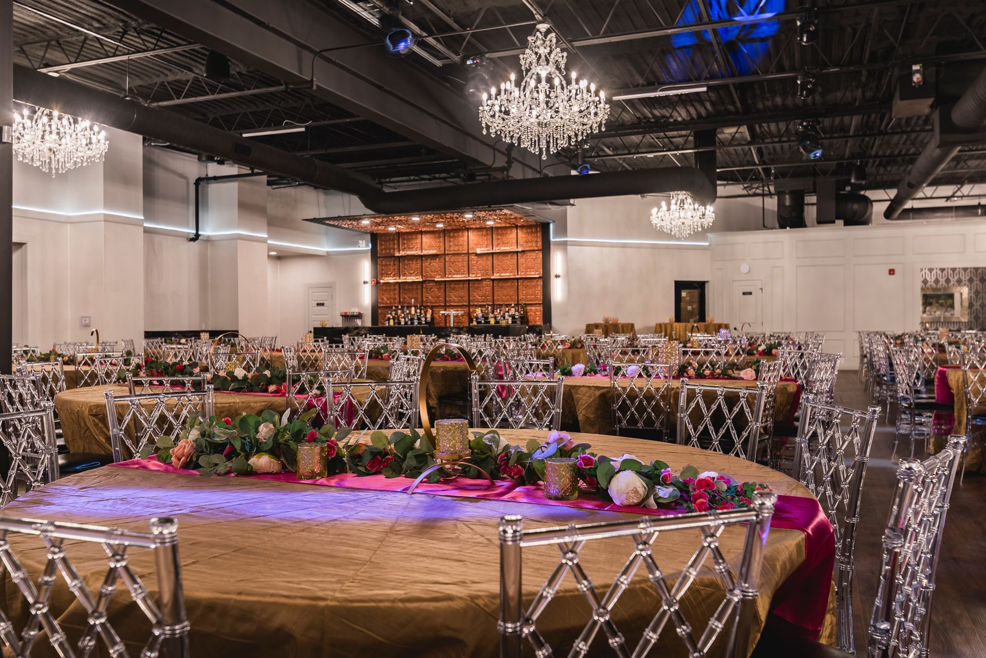 Elegant banquet hall with round tables, mirrored chairs, floral centerpieces, and chandeliers under a dark ceiling