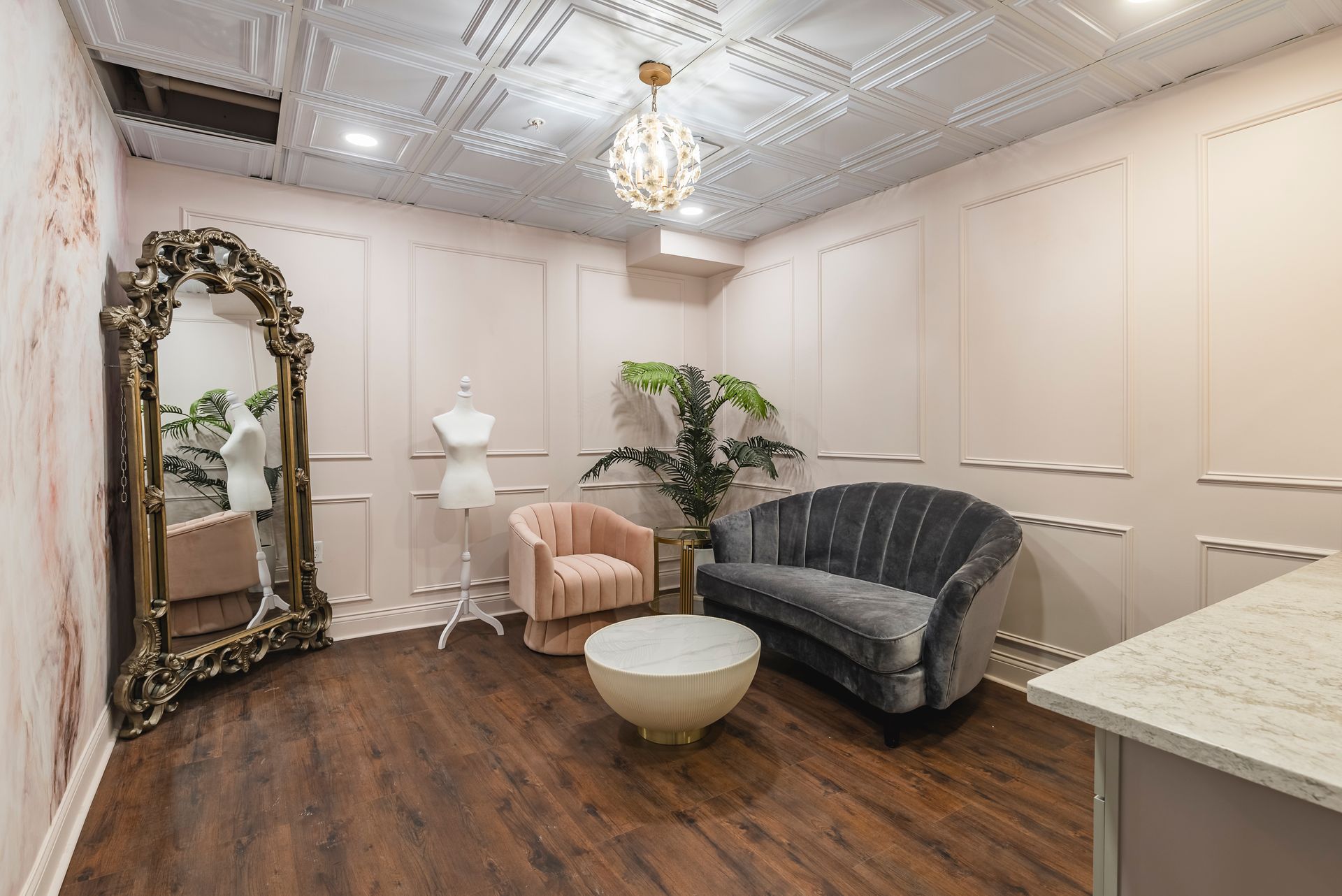 Elegant waiting room with pink walls, dark sofa, armchair, mirror, lamp, and chandelier lighting