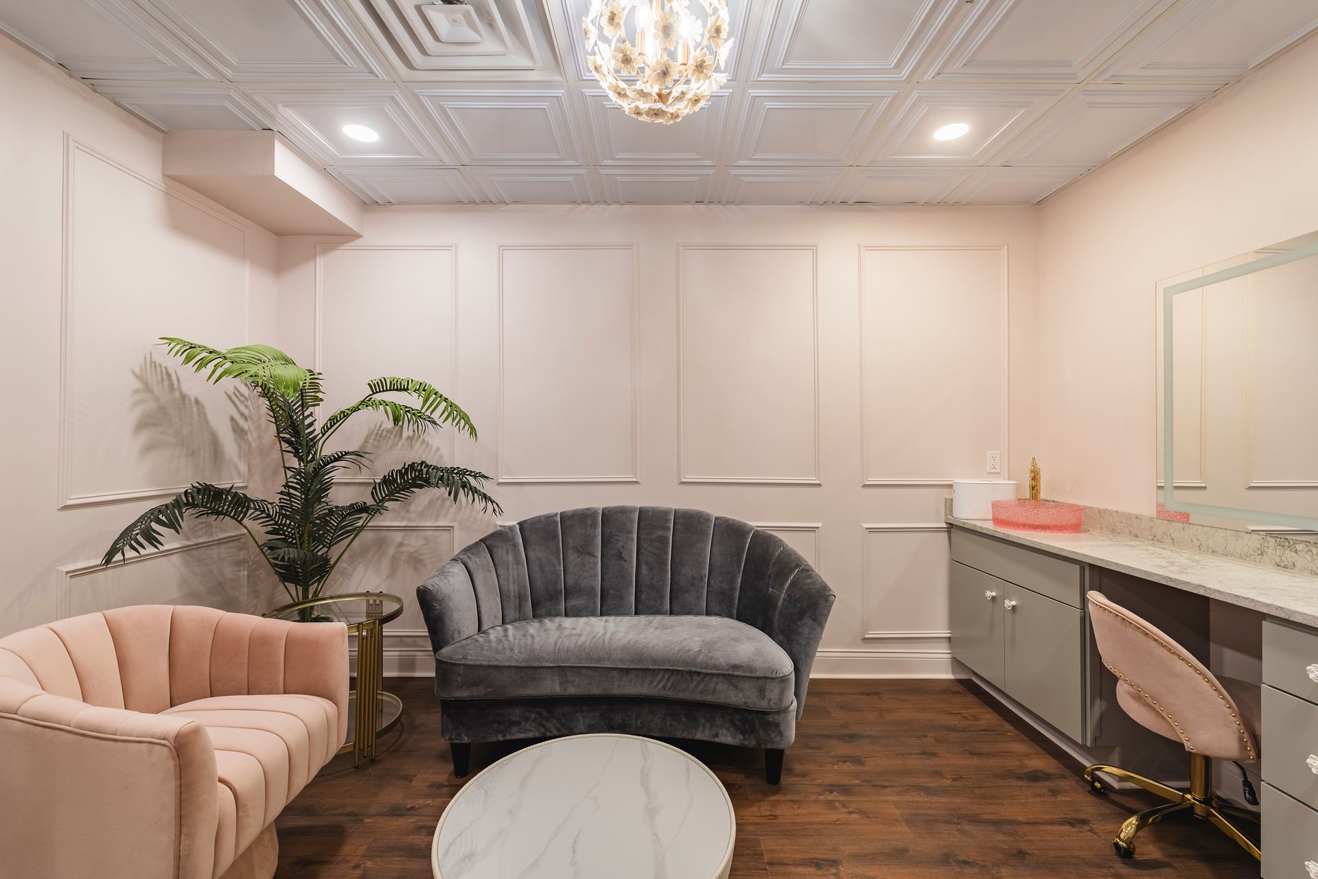 Elegant living room with blush and gray seating, white paneled walls, wood floor, and chandelier lighting