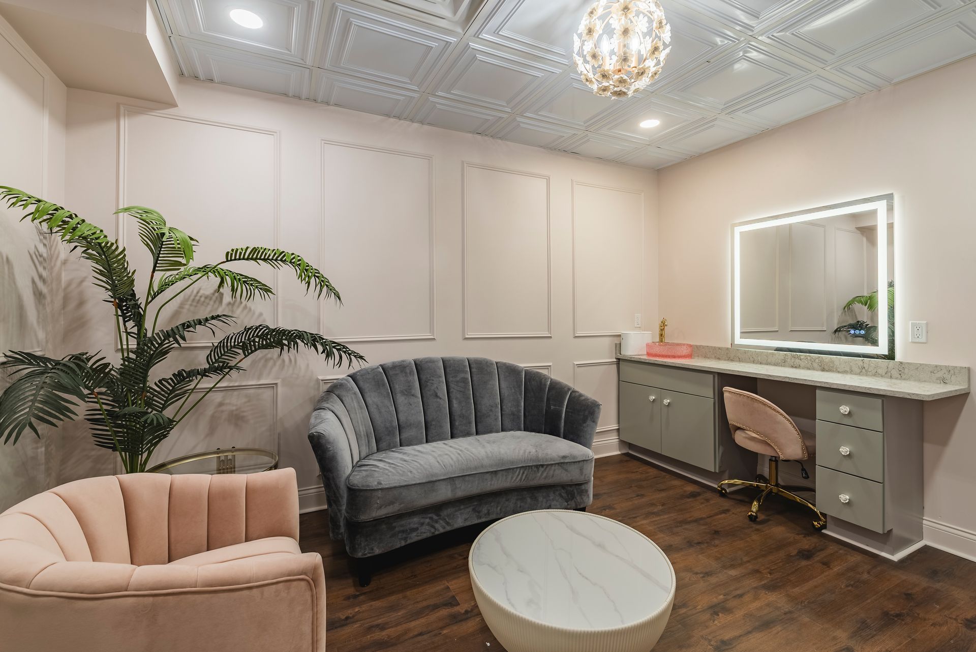Elegant dressing room with gray vanity, plush chairs, round table, and ornate ceiling lighting