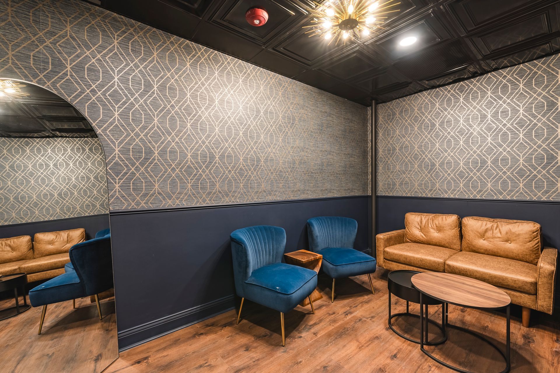 Cozy lounge with blue armchairs, tan sofa, patterned walls, and wood flooring in a dimly lit room