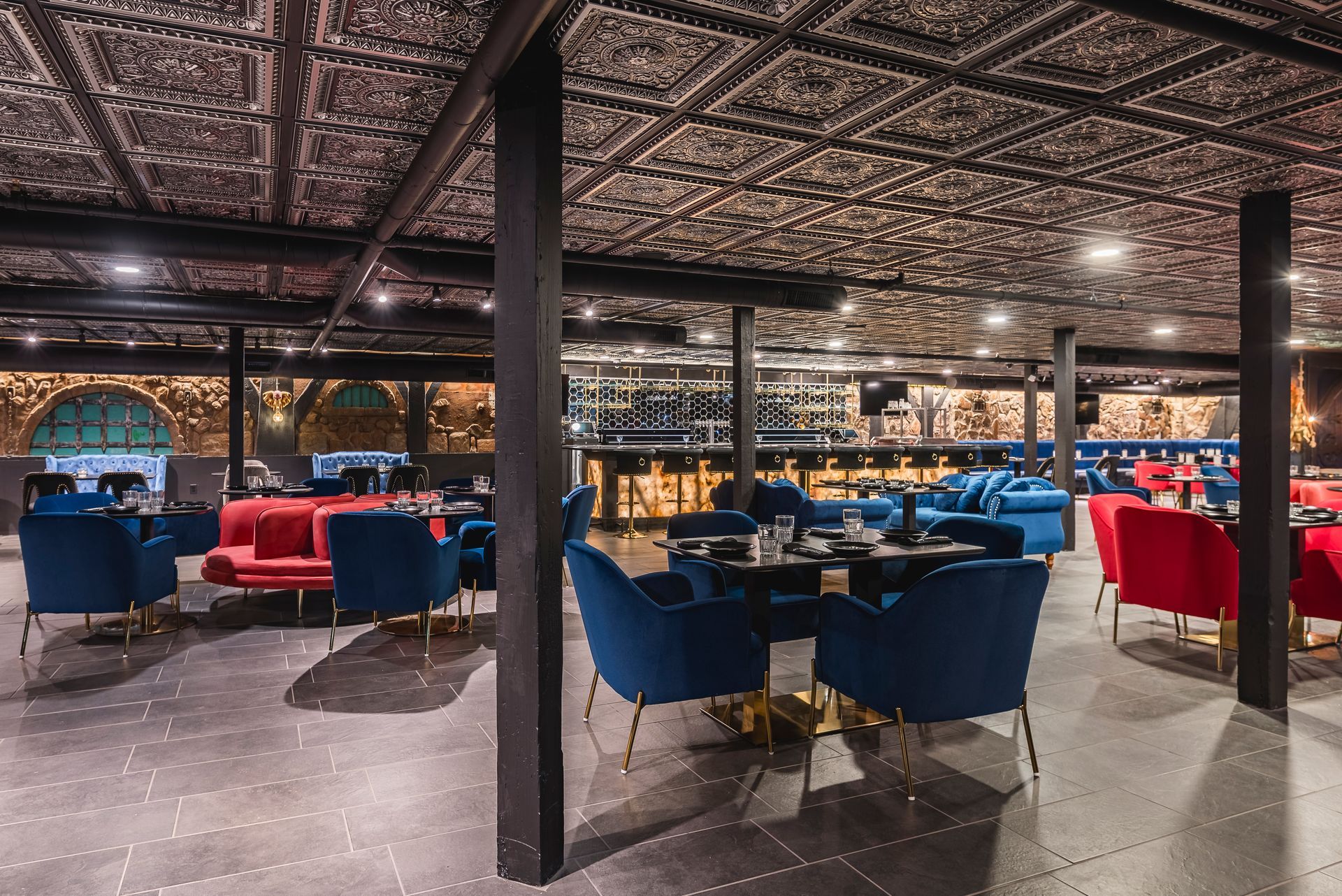 Elegant restaurant dining room with blue and red chairs, patterned ceiling, and warm ambient lighting