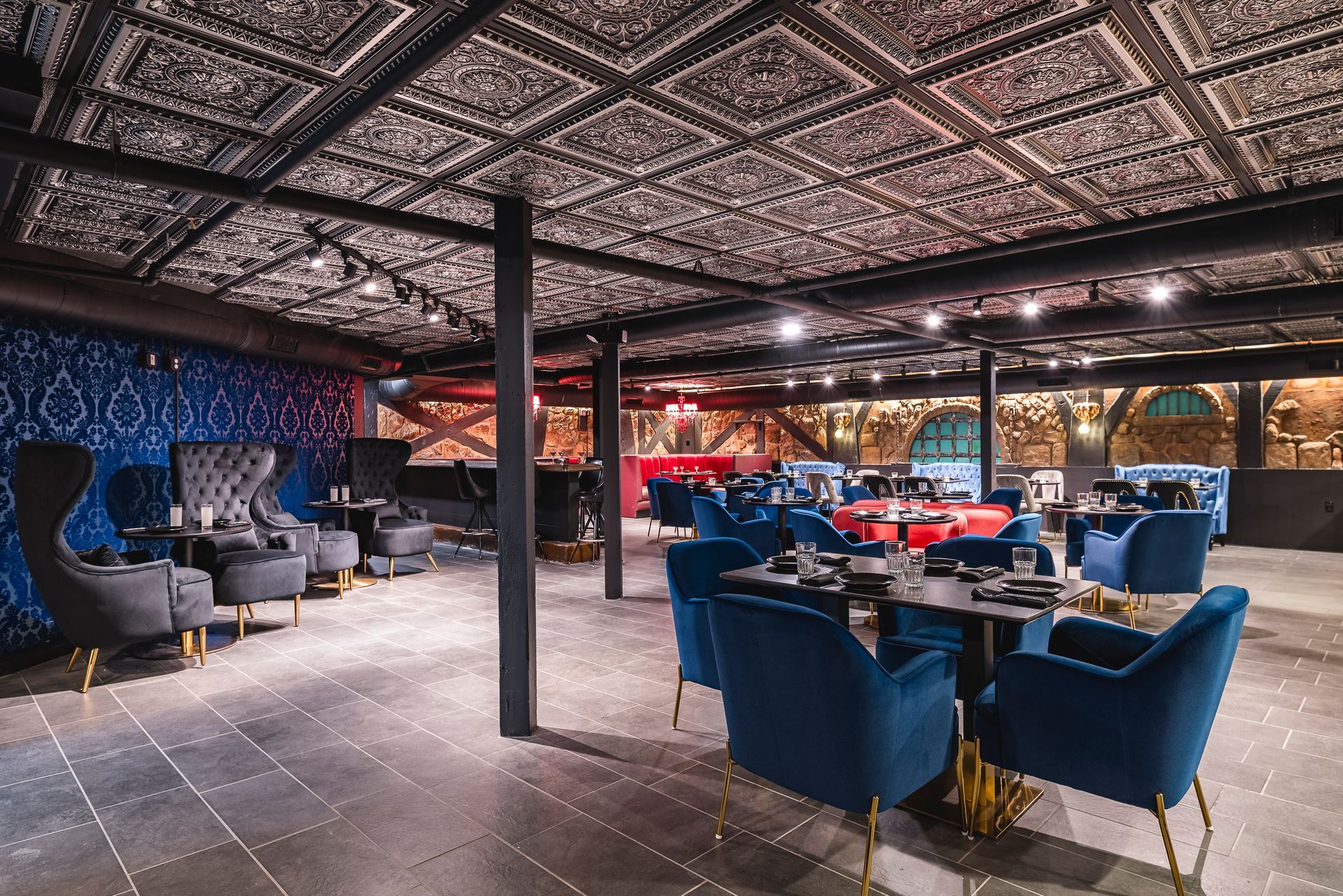 Modern lounge with blue chairs, tables, and patterned ceiling in a dimly lit interior
