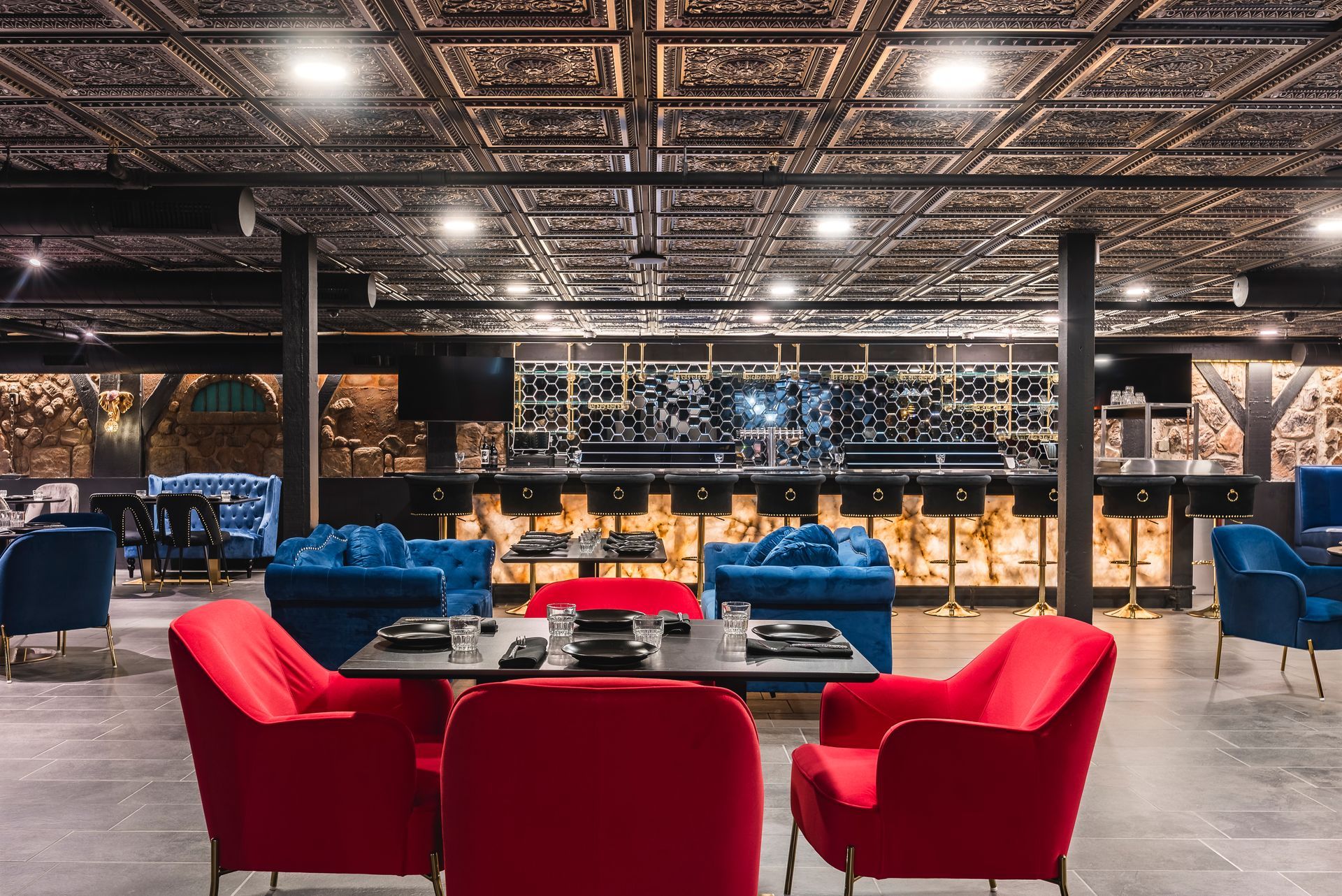 Stylish lounge with red and blue chairs, bar seating, and ornate ceiling lighting