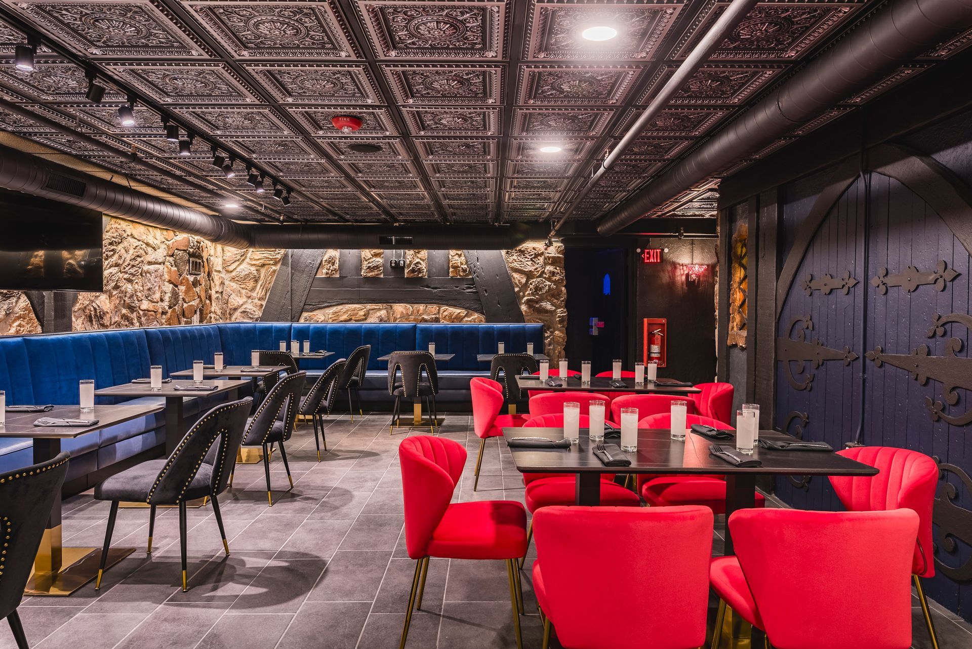 Modern restaurant interior with red chairs, black tables, and ornate patterned ceiling