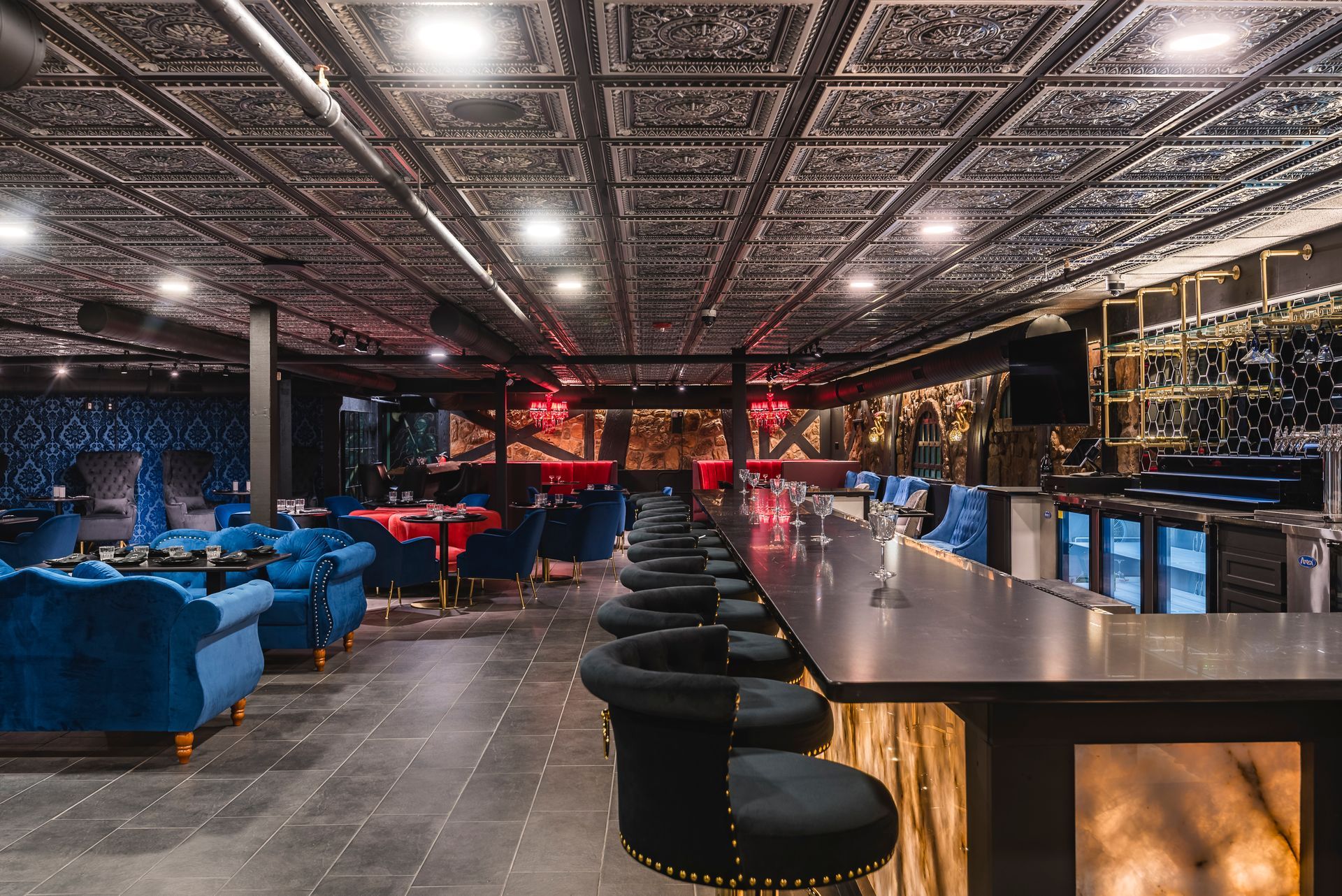 Modern lounge bar with blue sofas, round stools, and a long counter under patterned ceiling lights
