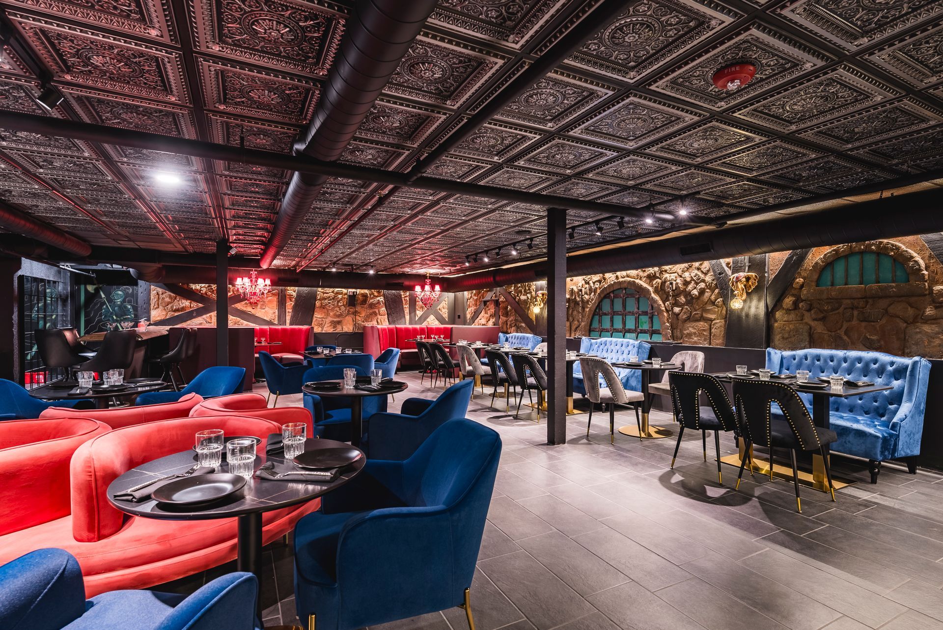 Stylish lounge with red and blue seating, patterned ceiling, and a bar area under warm lights