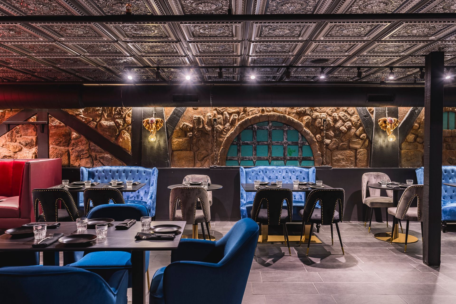 Elegant underground dining room with blue chairs, dark tables, brick walls, and warm accent lighting