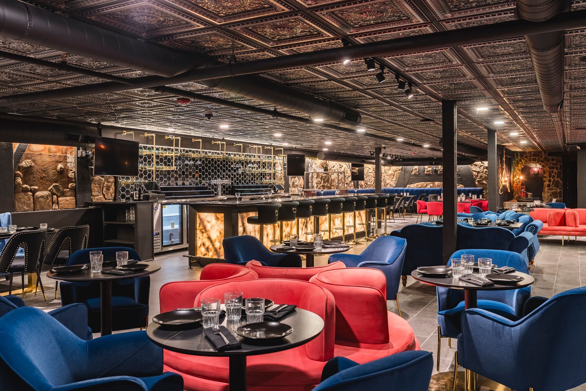 Dim nightclub/lounge interior with blue and red chairs, round tables, and ornate mirrored ceiling