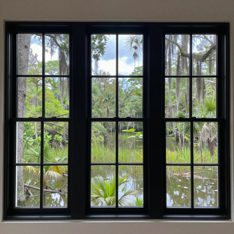 Black-framed window overlooking a bright green garden and pond