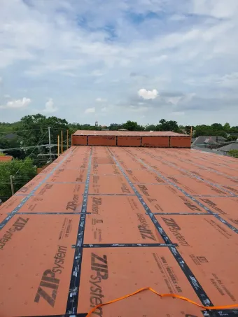Orange roof under construction with black underlayment, viewed toward a cloudy sky and nearby trees