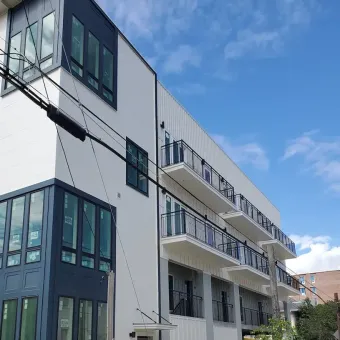 Modern white apartment building with blue-trimmed windows and balconies under a clear sky