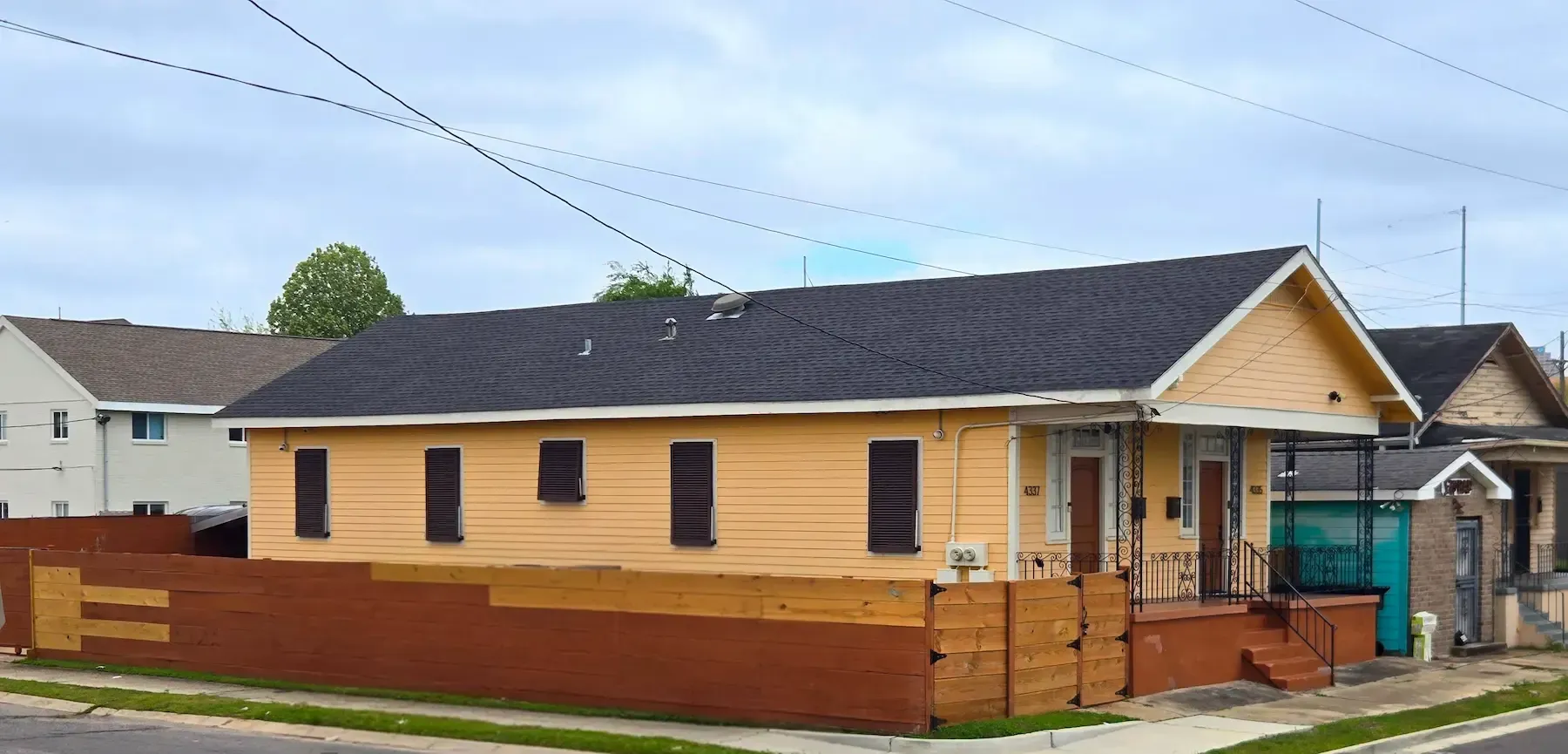 Single-story tan house with brown trim and a small fenced front porch on a residential street
