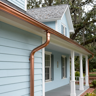Blue house exterior with copper gutter and downspout along a covered porch