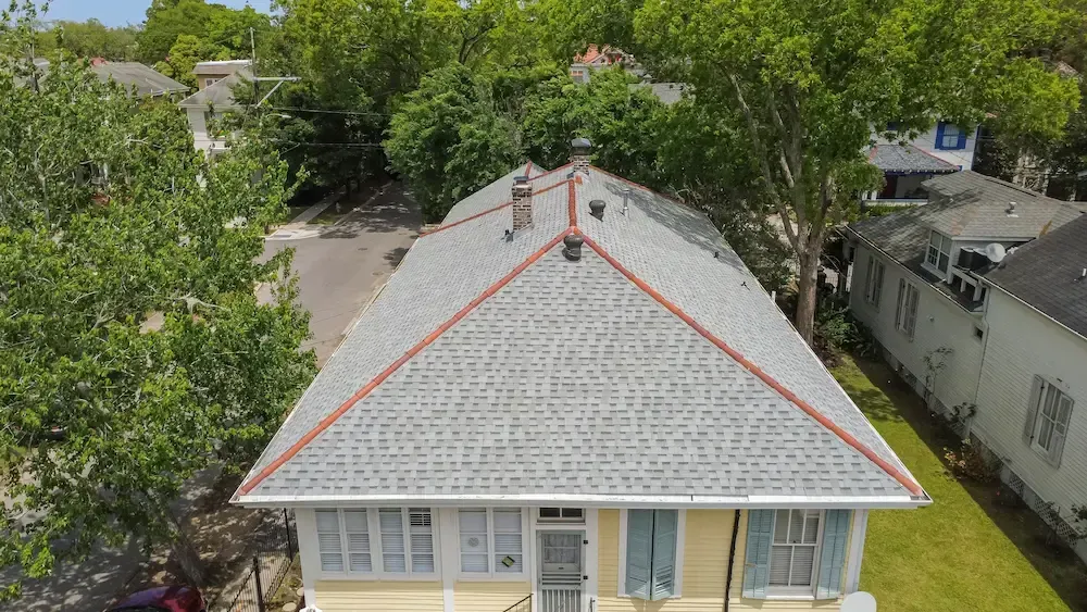 Aerial view of a house with a gray shingled roof, red trim, and trees surrounding it.