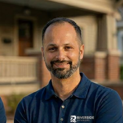 Smiling man in a navy Riverside polo standing outdoors in front of a house