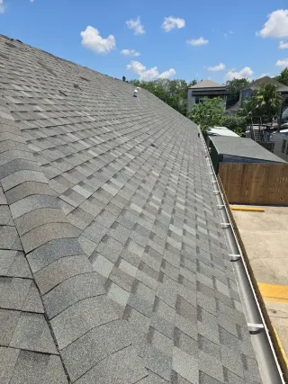 Damaged gray shingle roof on a house with missing shingles and visible repair materials