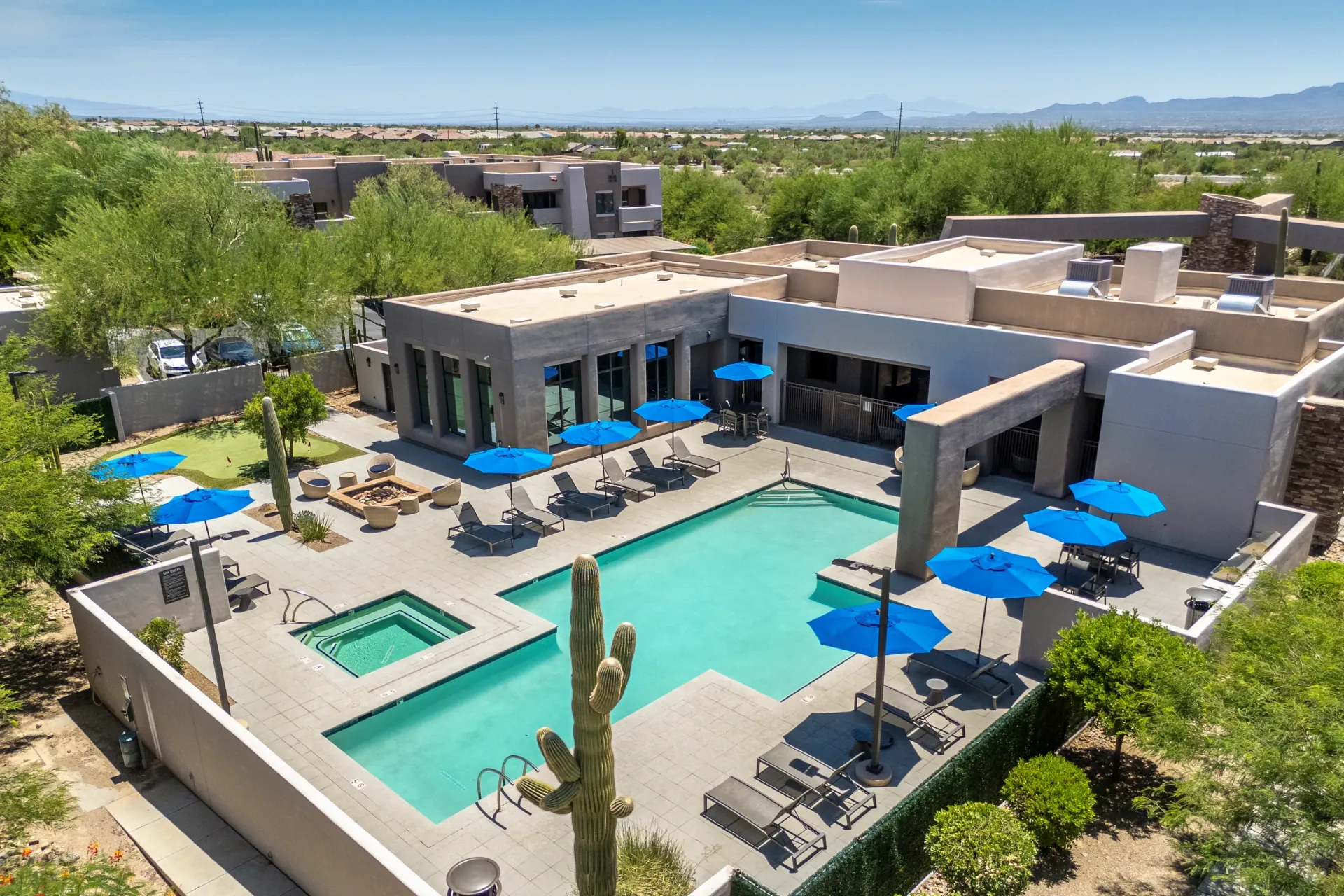 Aerial view of a resort-style swimming pool and spa area with lounge chairs and blue umbrellas.