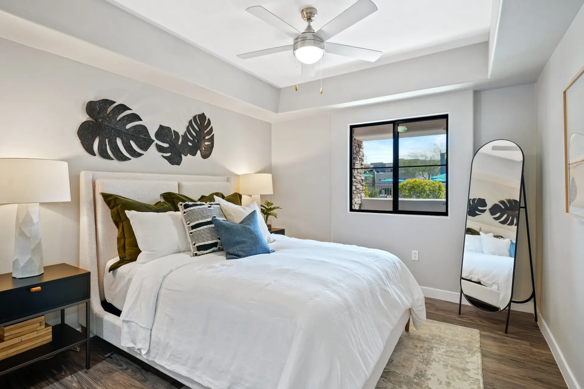 King-sized bed with white linens and decorative pillows in a bedroom with a ceiling fan and large mirror.
