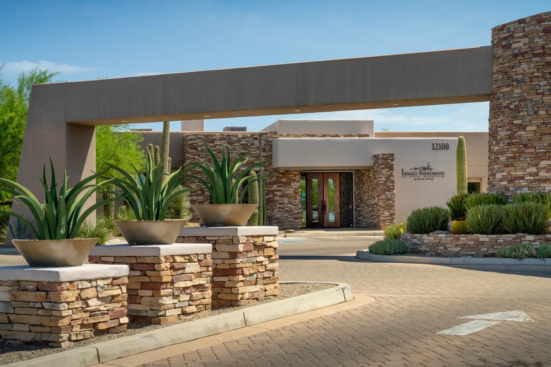 Entryway to Legacy Apartments at Dove Mountain, featuring stone pillars with plants and a modern archway.
