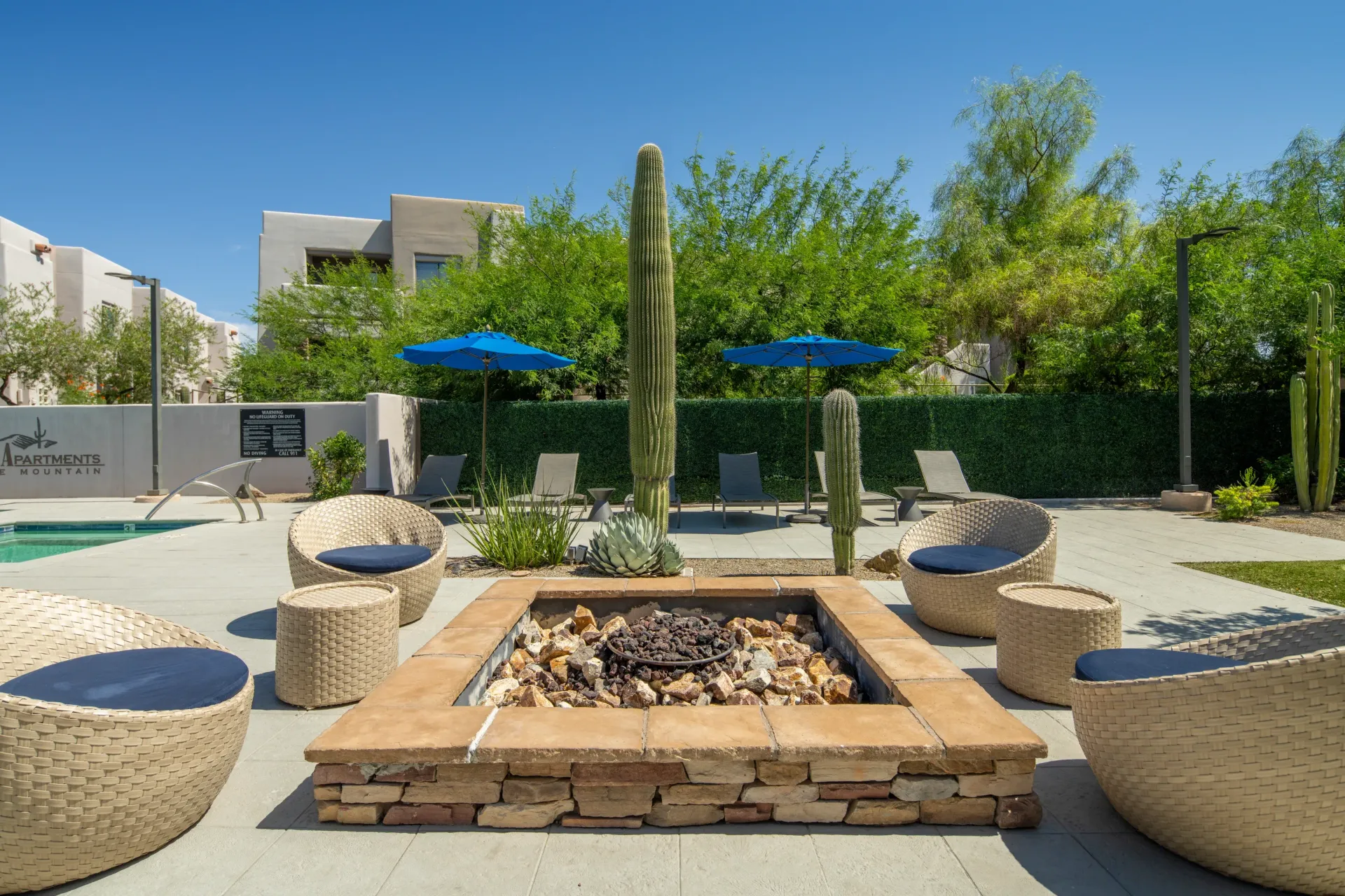 Apartment complex outdoor lounge area with a fire pit, seating, umbrellas, and pool.