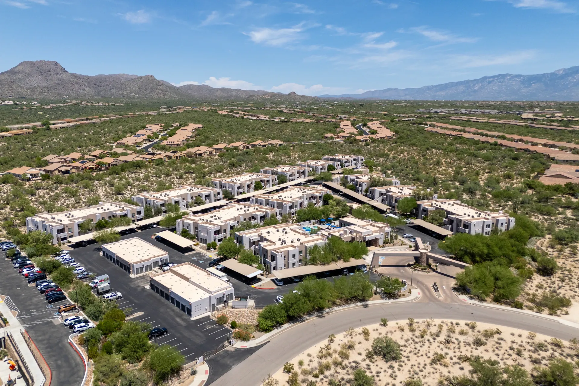 Aerial view of a multifamily property with multiple buildings and carports, set against a backdrop of desert mountains.