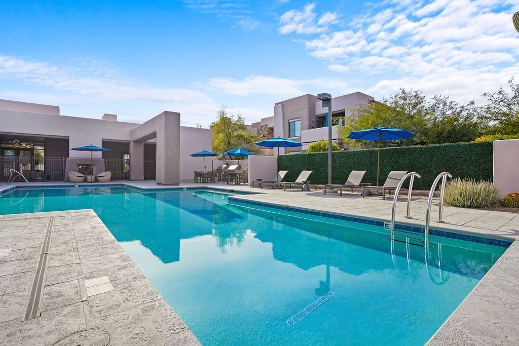 Outdoor apartment pool with blue umbrellas, lounge chairs, and a paved deck at Legacy Apartments at Dove Mountain in Marana, AZ.