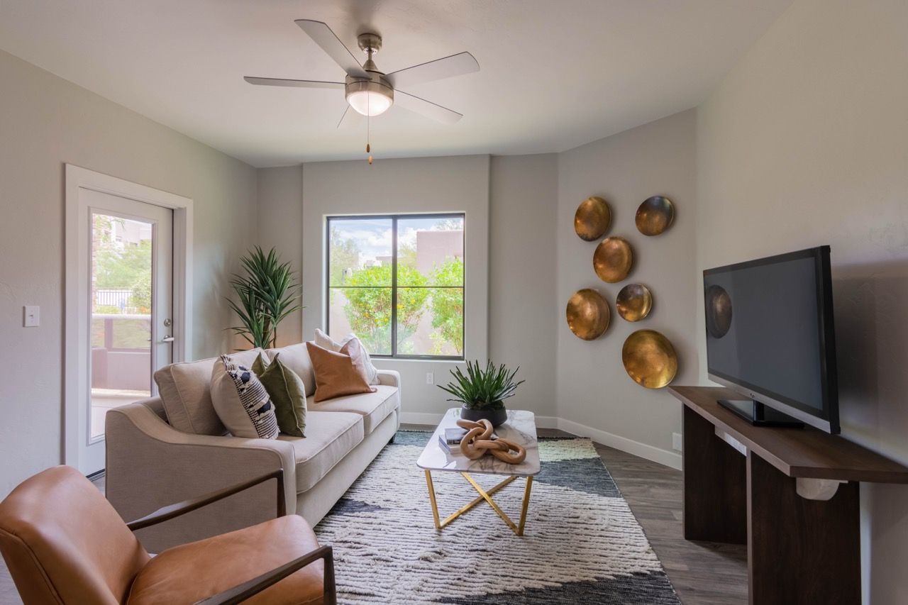 Living room in a modern apartment with a sofa, chairs, coffee table, wall decor, and a TV at Legacy Apartments at Dove Mountain in Marana, AZ.