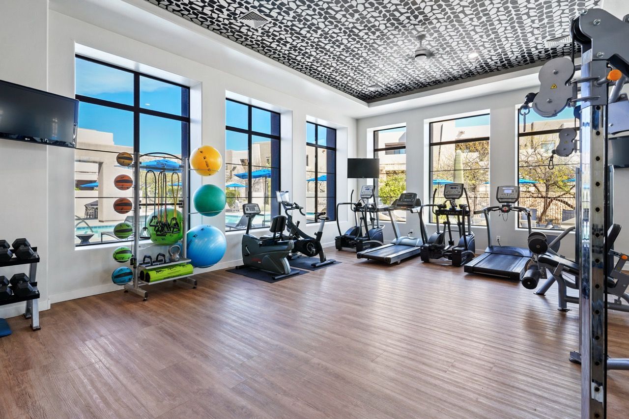 Bright on-site fitness center with treadmills, weights, and colorful exercise balls by large windows at Legacy Apartments at Dove Mountain in Marana, AZ.