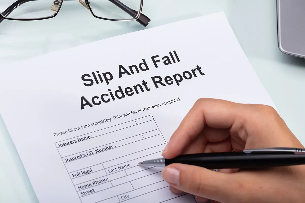 A person is writing a slip and fall accident report with a pen.