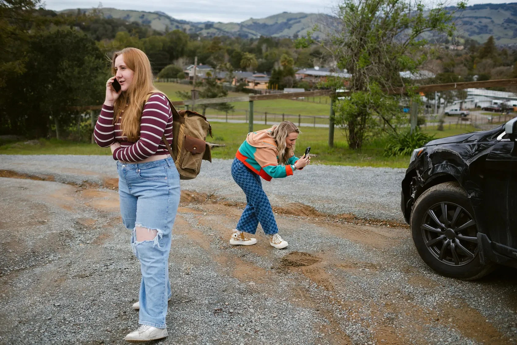 A woman is talking on a cell phone while another woman stands next to a car.