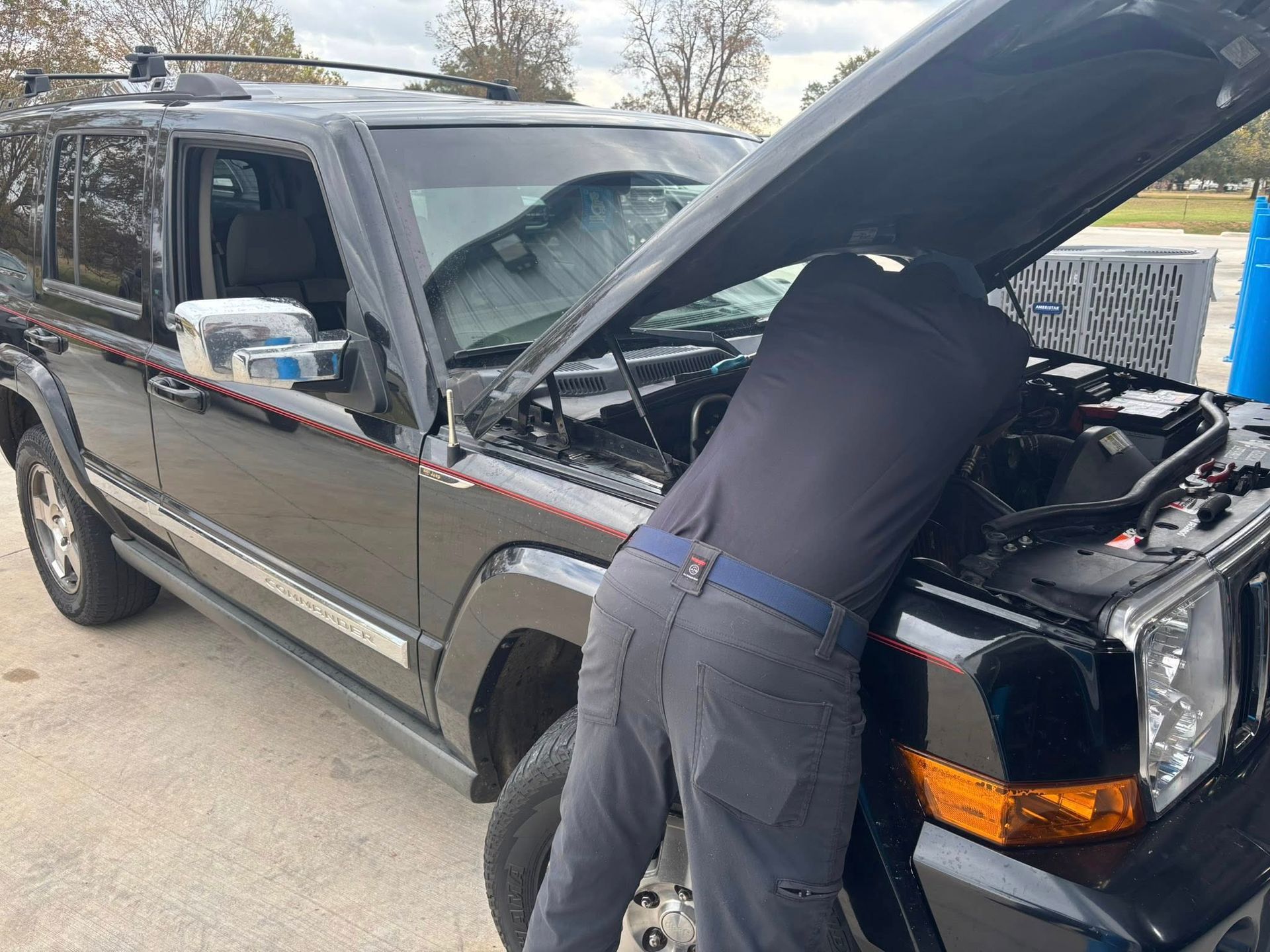 Person working under the open hood of a black SUV in a driveway