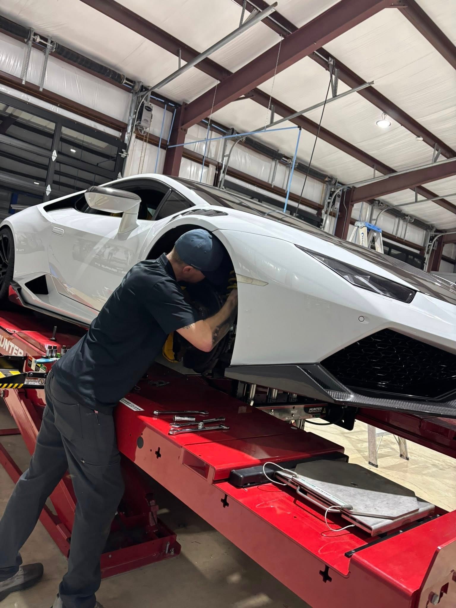 Mechanic working under a white sports car on a red lift in an auto shop