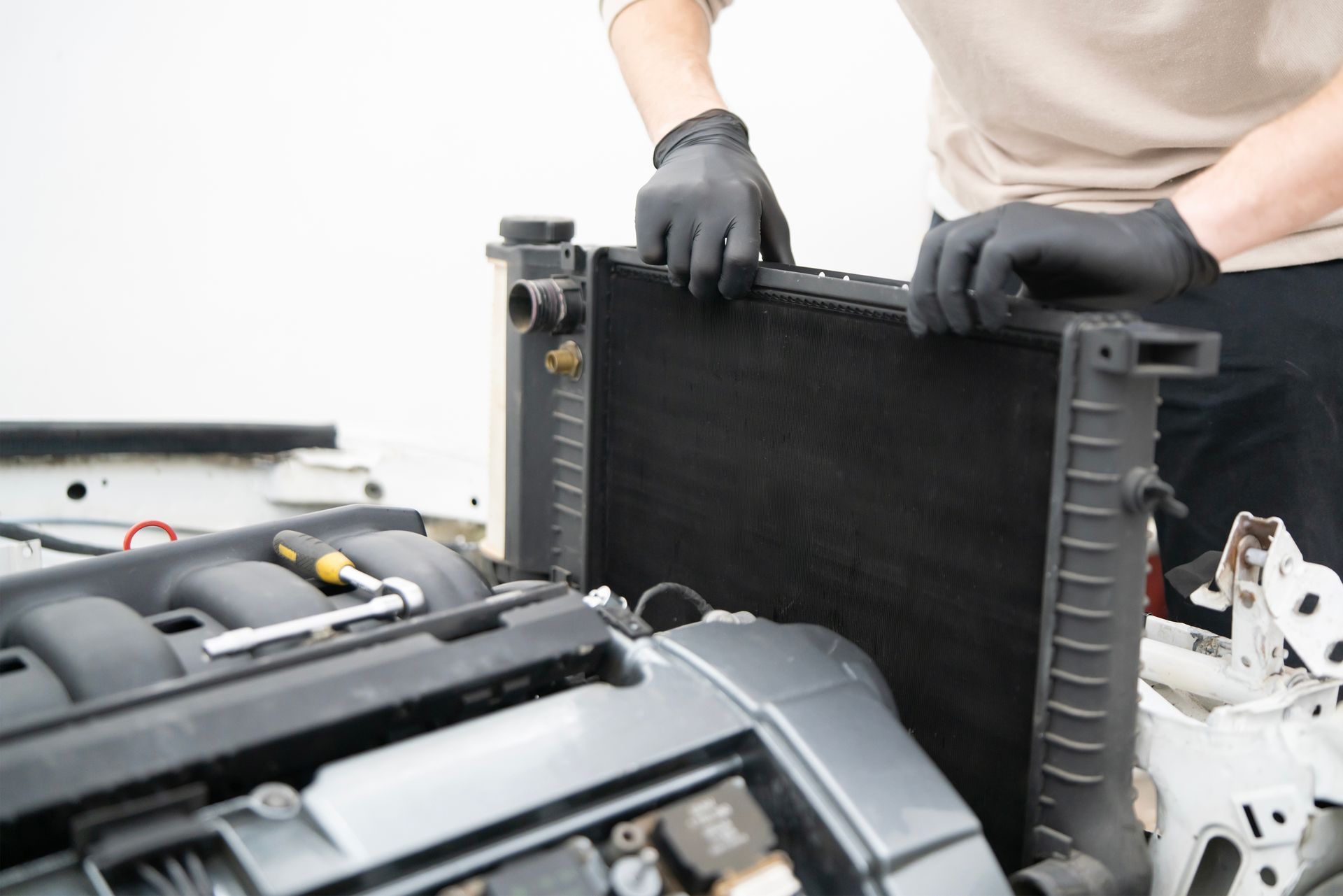 Gloved hands removing a car radiator during engine repair in a workshop