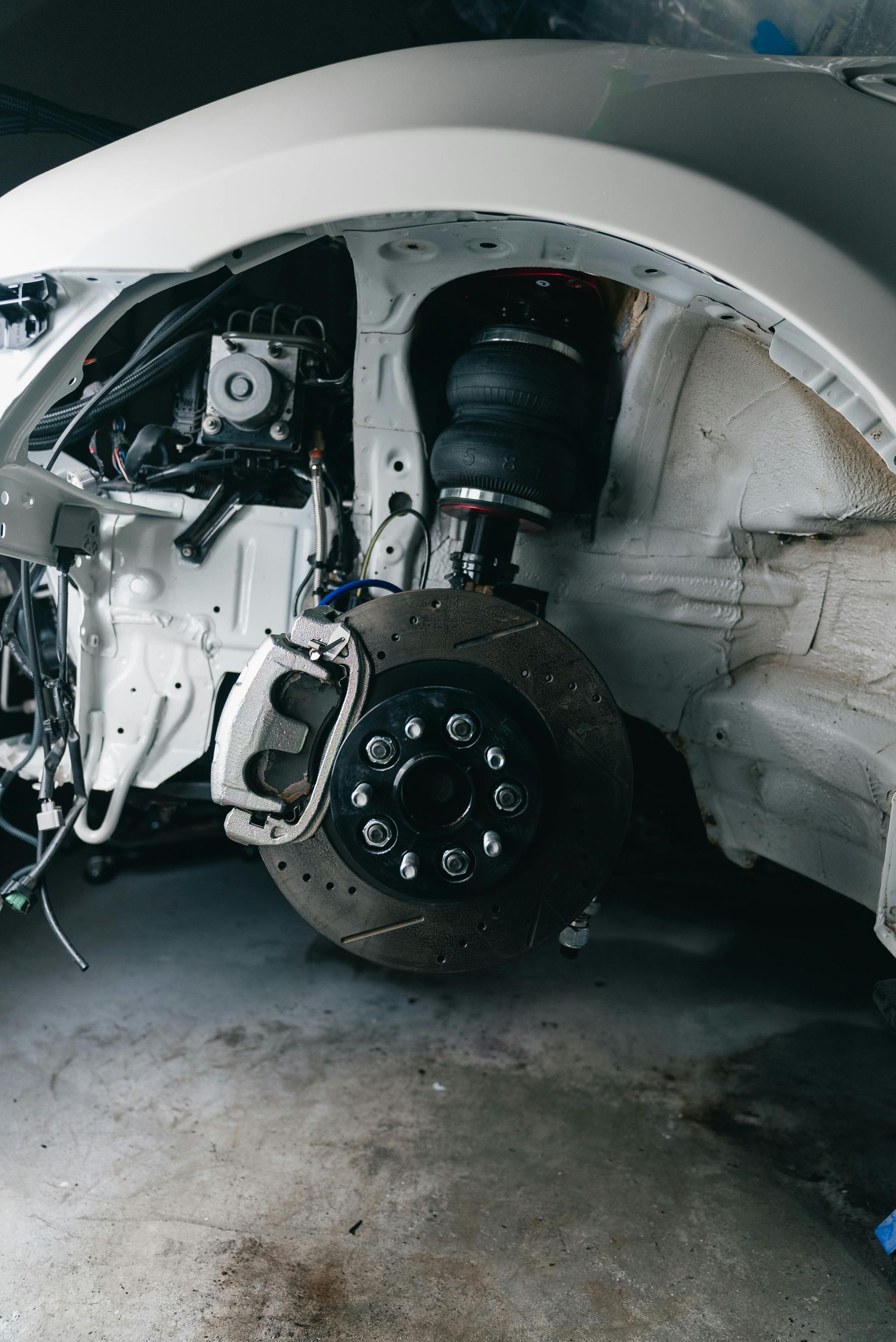 Car front wheel removed, exposing suspension and brake assembly in a garage