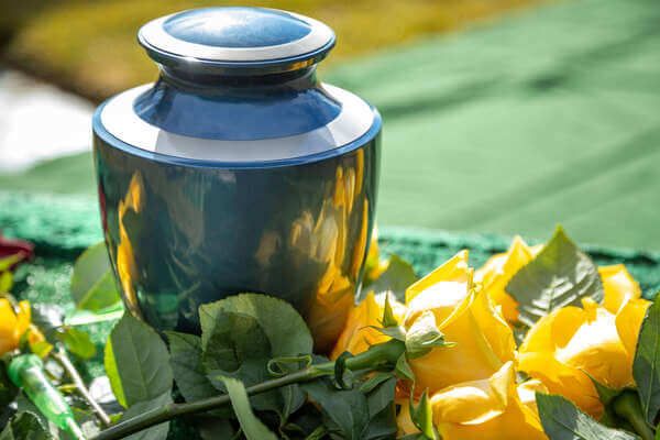 Blue urn surrounded by yellow roses and green leaves on a white cloth