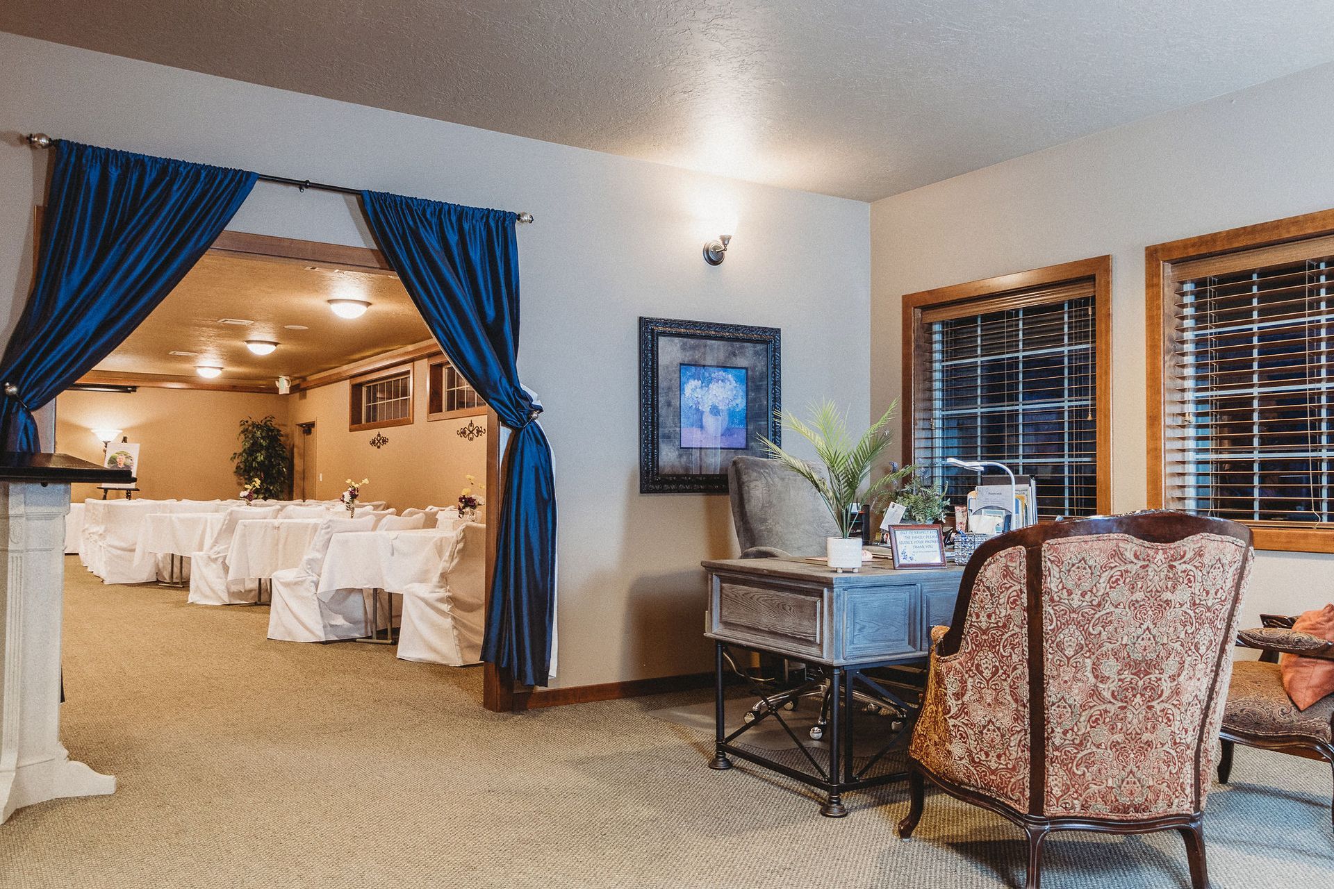 Elegant banquet hall with white-draped tables, blue curtains, and seating near a windowed lounge area