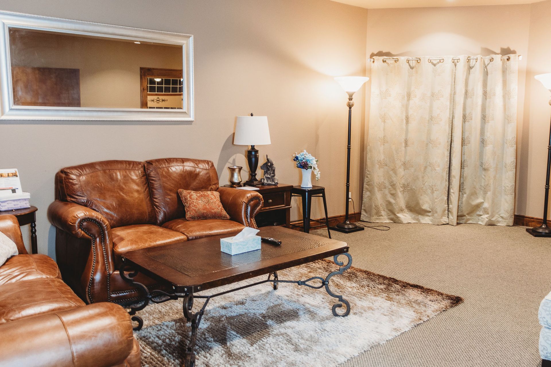 Cozy living room with brown leather sofa, coffee table, lamp, and beige curtains on a patterned rug