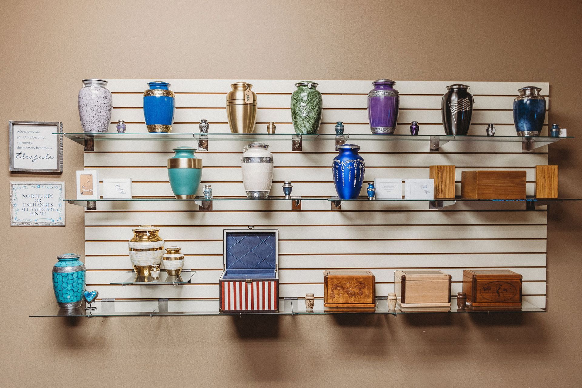 Wall display of colorful mugs, cups, and small wooden boxes on metal shelves against a beige wall